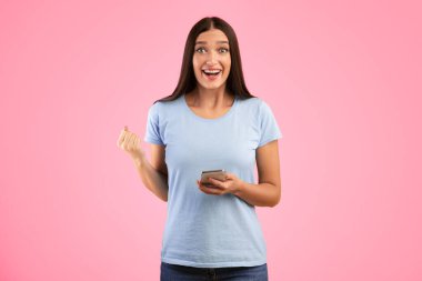 Öyle mi? Sarı stüdyo arka planında izole edilmiş akıllı telefon kullanan mutlu genç bir kadının portresi. Kazanmayı kutlayan heyecanlı bayan, sıkılmış yumruk, kameraya bakıyor.