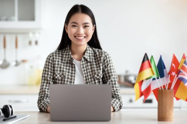 Güzel Asyalı kız öğrenci online okul arıyor, mutfakta dizüstü bilgisayarla oturuyor, fotokopi odası var. İnternette yabancı dil kursu arayan neşeli genç bir kadın. E-eğitim kavramı