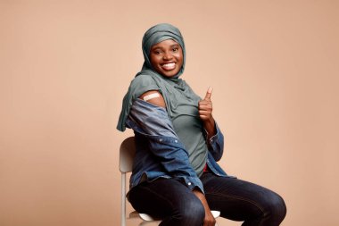 Antiviral bağışıklık sistemi, aşı. Siyah Müslüman Kadın, Covid-19 'a karşı aşılandı Aşılanmış Kol ve Bej arkaplandaki aşının kalitesini onaylayan jest gibi