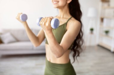 Covid karantina sırasında evde dambıllarıyla egzersiz yapan genç Hintli bayanın yakın çekimi, seçici odaklanma. Tanınmayan Asyalı kadın kol kaslarını güçlendiriyor, aile içi güç eğitimi alıyor.