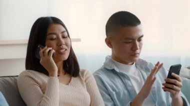 Genç bir adam ve bir kadın kanepede birlikte oturuyorlar, kadın telefonuyla konuşurken erkek akıllı telefonuna odaklanıyor. Pencereden güneş ışığı süzgeçleri.