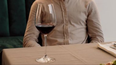 İyi giyimli bir insan, şık bir restoran masasında kaliteli şarapla çevrili güzel bir gurme yemeğinin tadını çıkarır ve unutulmaz bir yemek için davetkar bir ortam yaratır..