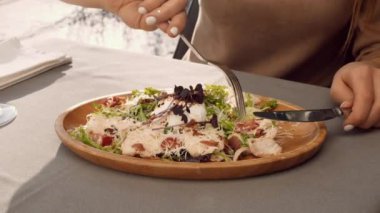 Bir insan güneşli bir günde açık havada taze yeşillik, peynir ve otlarla yapılan lezzetli bir salatanın tadını çıkararak enfes bir mutfak deneyimi sergiliyor..