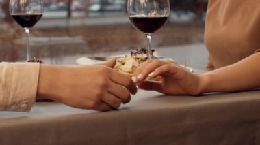 Bir çift sıcak bir masada oturuyor, bir tabak tatlı yerken el ele tutuşuyor ve kırmızı şarap yudumluyor. Günbatımının sıcacık parıltısı geceye romantik bir atmosfer ekler..