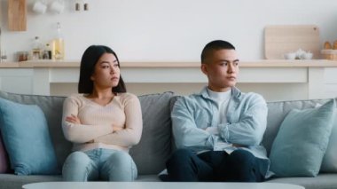 Kolları çapraz bir şekilde bir kanepede oturan bir çift anlaşmazlık belirtileri gösteriyor. Dekor, tarafsız renklerle ve asgari dekorla modern bir oturma odası..