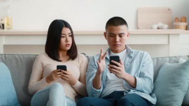 Sıcak bir oturma odasında, bir kadın akıllı telefonuna odaklanmış bir adamla konuşurken kaygılarını dile getirir. Atmosfer anlamlı bir konuşma ya da anlaşmazlık olduğunu gösteriyor..