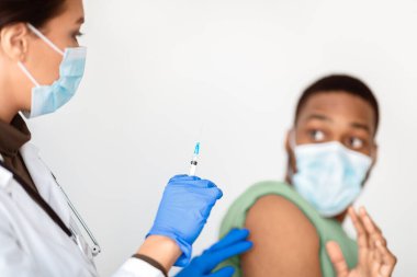 Siyahi Adam Covid-19 'a karşı aşılanmayı reddediyor, Beyaz arka planda şırınga pozu veren kadın doktoru durduruyor. Coronavirus aşısı korkusu. Kırpılmış, Seçici Odaklanma
