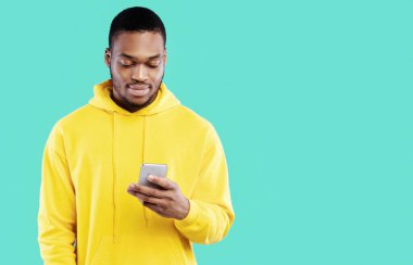 Sosyal medyada akıllı telefon mesajı kullanan ya da mavi stüdyonun arkasında duran sarı kapüşonlu yeni mobil uygulama kullanan siyahi bir genç. İnsanlar ve Gadget 'lar, Teknoloji Konsepti