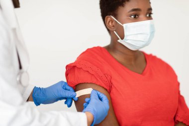 Coronavirus aşısı. Afrika kökenli Amerikalı bir kadın kovid 19 virüsüne karşı antiviral aşı aşısı oluyor, hemşire koluna bandaj yapıştırıyor, beyaz arka plan. Kırpılmış