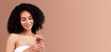 African American woman enjoys her beauty routine, applying skin care serum while smiling. She is isolated against a soft, empty background, embracing the art of self-pampering at home. clipart