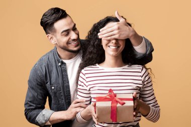 Sürpriz Hediye. Romantik Arap adam sevgilisinin gözlerini kapatıyor ve hediye veriyor. Karısını doğum günüyle, evlilik yıldönümüyle ya da sevgililer günüyle karşılıyor. Sarı arka planda duruyor.