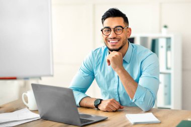 Mutlu Arap iş adamının portresi dizüstü bilgisayar kullanıyor, video görüşmesi yapıyor, ofisteki meslektaşımla internette sohbet ediyor. Genç girişimci sanal toplantı mı yapıyor yoksa iş sitesi mi?