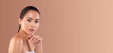 Asyalı bir kadın, minimalist bir ortamda kendini şımartırken ve rahatlatırken bir cilt bakım ürünü uyguluyor. Yumuşak arka plan doğal güzelliğini ve bakımını arttırıyor..