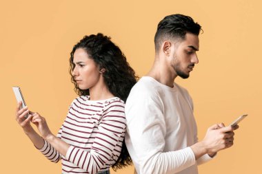 Gadget Bağımlılık Konsepti. Sırt sırta duran ve akıllı telefonlar kullanan genç bir Arap çift Orta Doğulu erkek ve kadın cep telefonlarıyla zaman geçirirken birbirlerini görmezden geliyorlar.