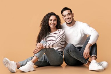 Mutlu genç Arap çiftin portresi sarı arka planda poz veriyor, neşeli ortaçağ erkek arkadaşı ve kız arkadaşı stüdyoda oturuyor ve kameraya gülümsüyor,