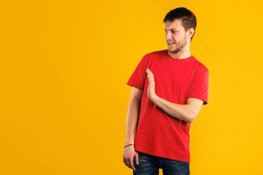 Mesafeni koru, bana yakın durma. Yüzünde tiksinti ifadesi olan, el kaldıran, avuç içiyle dur hareketi yapan, mavi stüdyo arka planında tek başına duran genç adam.