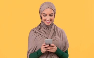 Çevrimiçi cep telefonu mesajları kullanan neşeli Arap Kadın Stüdyodaki sarı arka planda duran sosyal medyada iletişim kuruyor. Happy Smartphone Kullanıcısı, Cep telefonu Uygulaması Reklam Kavramı