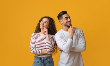 Dalgın Arap erkek ve kadın bir şey düşünüyor ve uzaklara bakıyor, düşünceli orta doğu çifti çenelerine dokunuyor ve sarı arka planda birlikte poz verirken gülümsüyor,