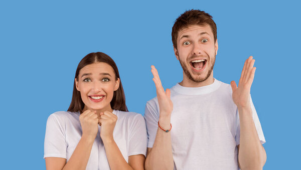 Возбужденная молодая пара счастливо кричит в камеру, держа руки поднятыми, фиолетовый фон
