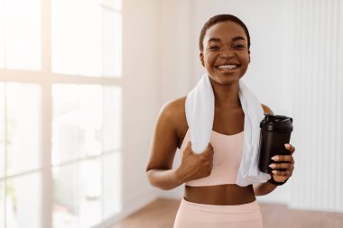 Beyaz spor kıyafetleri içinde güzel, gülümseyen bir kadın portresi ve sağlıklı içeceklerle sallanan bir havlu, beyaz protein, temiz su ya da kahve izole edilmiş bir şekilde kameraya bakarak poz veren bir havlu.