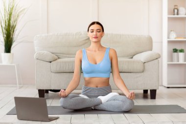 Çevrimiçi Yoga dersinde meditasyon yapan barışçıl bir kadın dizüstü bilgisayarda oturuyor ve evde dinleniyor. Rahatlama Egzersizi Konsepti