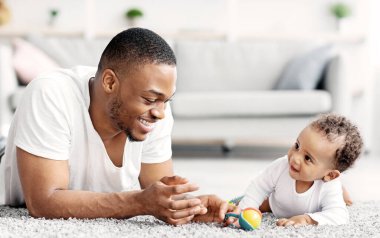 Baba-bebek bağı. Genç, mutlu zenci babanın evde oğluyla oynadığı portresi, tatlı Afrikalı küçük Amerikalı çocuk babasıyla oturma odasında dinleniyor, birlikte vakit geçiriyor.