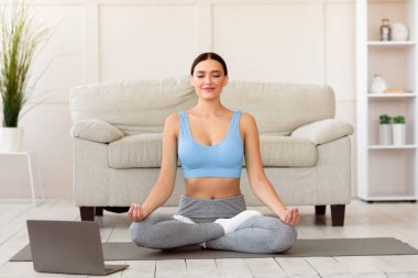Çevrimiçi yoga. Evde Lotus pozisyonunda oturan sakin kız laptopta dinleniyor..