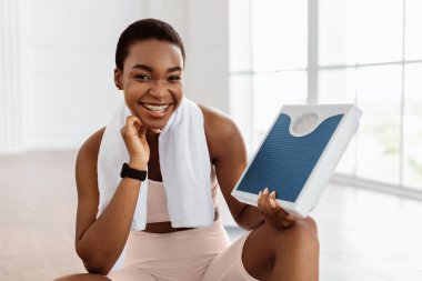 Diş teli takan heyecanlı sporcu kadının portresi evde ya da fitness stüdyosunda, diyet ve egzersizlerinden memnun, kameraya bakıyor. Kilo verme hedefine ulaşan neşeli bayan, başarı