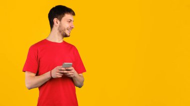 İletişim ve Teknoloji. Mavi stüdyo arka planında izole bir şekilde duran akıllı telefonunu kullanan gülümseyen adamın portresi, fotokopi alanına bakıyor, elinde aletlerle. İnternette sohbet eden adam.