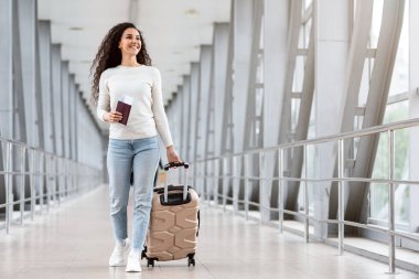 Havaalanı Terminali 'nde bavulunu elinde tutan ve uçuş kapısına giderken bavulunu taşıyan neşeli Orta Doğu kadını ile birlikte yürüyen mutlu bir genç kadın.