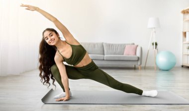 Genç Hintli kadın yoga ya da pilates yapıyor, ev içi eğitim sırasında kollarını ve bacaklarını esnetiyor, fotokopi çekiyor. Sportif Asyalı bayan esnek egzersizler yapıyor, evde sağlıklı bir yaşam sürüyor.