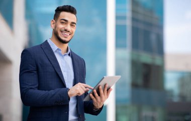 Resmi görevdeki yakışıklı Arap adam ofis binasının yanında dikiliyor, dijital tablet tutuyor ve gülümsüyor, internetten yeni iş fırsatları arıyor, iş başvurusu, fotokopi alanı, panorama kullanıyor.