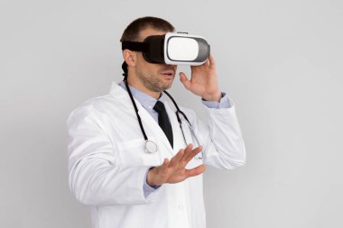 VR Tıp. Tıbbi Amaçlar İçin Sanal Gerçeklik Kulaklığı Kullanan Erkek Doktor Beyaz Stüdyo Arkaplanının Üzerinde Durmakta