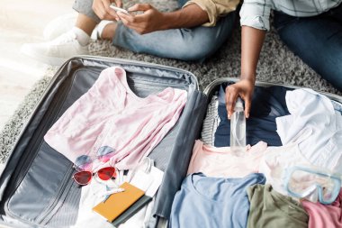 Covid-19 salgını sırasında iyi tatiller. Tanınmayan siyah aile çifti dezenfektan bavullarını evde geziye hazırlanıyor. Modern Turizm ve Seyahat. Kırpılmış, Yüksek Açı Atışı