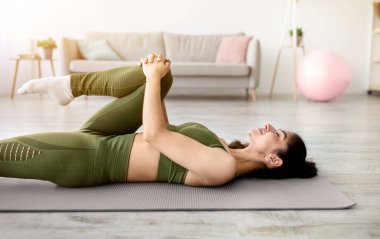 Fit Hintli kadın evde paspasın üzerinde yatarken bacağını esnetiyor. Doğulu kadının esneklik egzersizleri yaparken, yoga ya da pilates yaparken, aktif bir yaşam tarzı sürerken yan görüntüsü. Yurt içi eğitimler