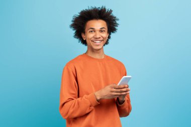 Kıvırcık saçlı neşeli bir milenyum adamı, akıllı telefonuyla meşgul olan mavi bir fon karşısında duruyor. Turuncu bir kazak giyiyor ve bağlı anların tadını çıkarırken rahatlamış görünüyor..