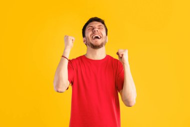 Kazanan Kavram. Stüdyo portresi, mavi arka planda izole bir şekilde havaya kaldırılmış yumruklarla bağıran genç bir adam. Heyecanlı adam tezahürat yapıyor, bağırıyor, zaferi kutluyor.