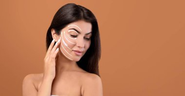 Uzun siyah saçlı bir kadın, izole bir ortamda güzelliğini geliştiriyor. Yüzüne nazikçe bir cilt bakım ürünü uyguluyor, rahatlatıcı hareketlerle şımartıcı bir rutini teşvik ediyor..