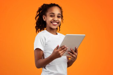 E-öğrenme. Dijital tablet kullanan mutlu Afrika kökenli Amerikalı kız. İnternette ödev yapıyor. Sarı Stüdyo 'nun arka planında tek başına duran kameraya bakıyor. Boş Alanı Olan Pankart