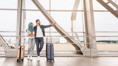 Birlikte seyahat ediyoruz. Mutlu Müslüman eşler havaalanında bavullarıyla bekliyor, neşeli orta doğu çifti terminalin yanında bekliyor, adam işaret ediyor, boşluğu kopyalıyor.