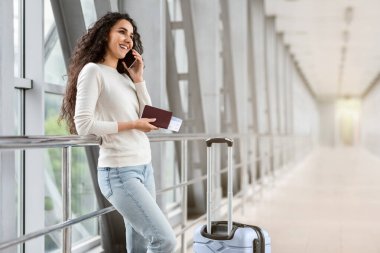 Havaalanında çantalarla beklerken cep telefonuyla konuşan güzel esmer bayan, Milenyum Orta Doğulu Kadın Terminal 'de duruyor ve keyifli cep telefonu konuşmaları yapıyor, Boşluğu Kopyala