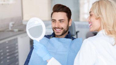 Mutlu genç hasta için ayna tutan neşeli doktor dişçi diş hekimi, doktor ve hasta diş tedavisi sonuçlarını kontrol ediyor aynaya bakıyor ve gülümsüyor, panorama, kopyalama alanı