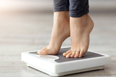 Kapalı alanda ağırlığını ölçen, terazinin üzerinde duran genç Hintli bir kadın. Tanımlanamayan milenyum hanımefendisi zayıflama sürecinin sonuçlarını kontrol ediyor.