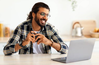 İnternette iş arayan neşeli Hintli adam, masada oturuyor, dizüstü bilgisayar kullanıyor, kahve içiyor, mutfak içi, fotokopi odası. Evden çalışan mutlu Arap erkek öğrenci, uzaktan çalışma.