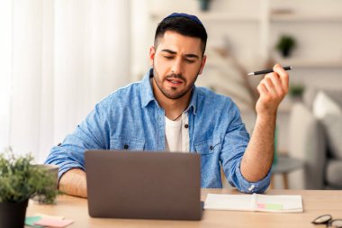 Çevrimiçi Uzaktan İletişim Konsepti. Kippah 'ta video konferansında sanal toplantı yapan odaklanmış Yahudi erkek işçinin portresi. Ciddi bir adam ofis masasında oturmuş fikirleri tartışıyor.