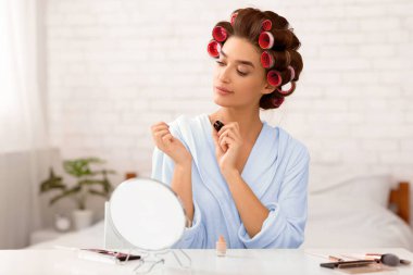 Manikür. Göz kamaştırıcı ev hanımı tırnak cilası sürerken evde, yatak odasında oturuyor, bigudilerle kıvırcık saçlı. Kadın Güzellik Hizmetleri rutini. Seçici Odaklanma