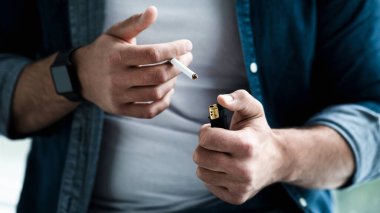 Evde sigara içen bir adam. Nikotin bağımlılığı, zihinsel sorunlar ve sorunlar, kötü alışkanlık ve endişe. Üzücü mutsuz Avrupalı adam sigara yakıyor, kırpıyor, kapıyor, boşluğu dolduruyor.