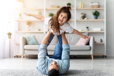 Mutlu bir ortadoğulu baba ve kızı evde uçakla oynarken, genç Arap babası gülen kızını kaldırıyor, rahat bir oturma odası, fotokopi alanı, babalık kavramı.