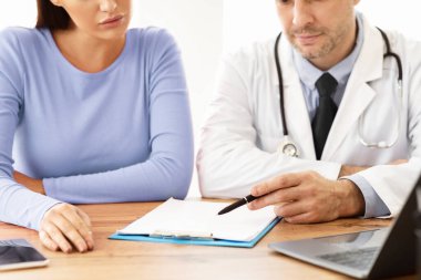 Genel Uygulayıcı Randevusu. Hastasına teşhisi ve tedaviyi tartışan erkek doktor çizelgesini gösteriyor. Ofisinde masasında oturan bir kadına danışmanlık yapan bir uzman.