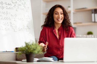 E-Öğrenme Konsepti. Gülümseyen kadın matematik öğretmeni konuşuyor, videodaki öğrencilere trigonometrik fonksiyonları açıklıyor. Heyecanlı kadın dizüstü bilgisayara bakıyor, masada oturuyor.